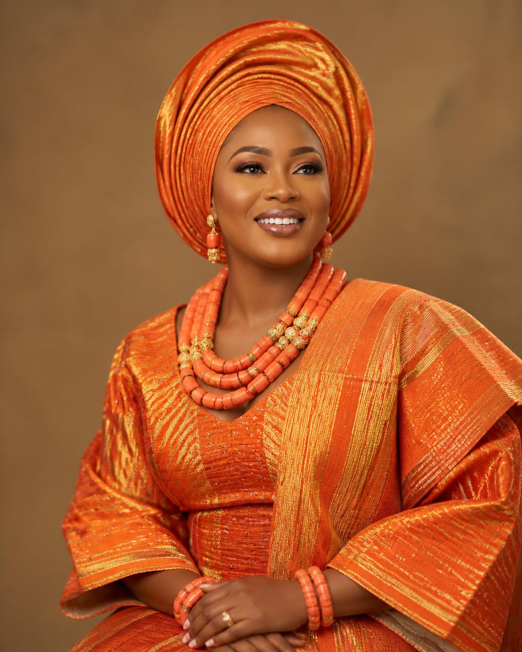 Woman wearing orange and gold aso-oke iro and buba with tied gele